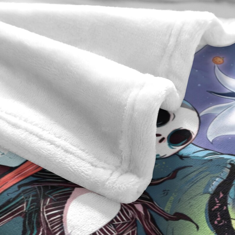 May include: A white plush blanket with a detailed illustration of Jack Skellington from The Nightmare Before Christmas. The blanket features a soft, folded edge and a colorful design with a purple and blue background.