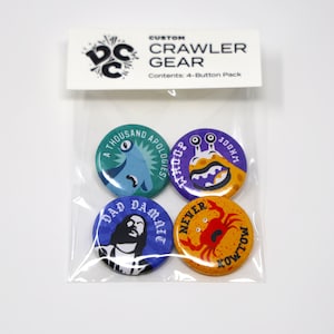May include: A clear plastic bag containing a 4-button pack. The buttons are round and feature various designs and text, including a blue monster, a crab, and the words "DAD DAMAGE". The top of the bag has a white label with the text "CUSTOM CRAWLER GEAR".