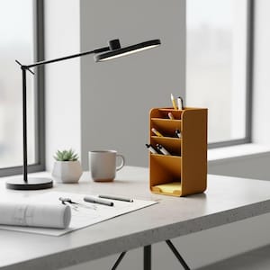 Può includere: Un moderno allestimento da scrivania con una lampada da scrivania nera, un organizer da scrivania giallo senape, una piccola pianta grassa in un vaso bianco e una tazza grigia. L'organizer contiene penne, matite e un blocco note. Progetti architettonici e strumenti di disegno sono sulla scrivania.