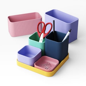 Könnte beinhalten: Ein farbenfrohes Schreibtisch-Organizer-Set mit Behältern in Rosa, Grün, Blau und Lila. Das Set enthält ein gelbes Tablett, eine rote Schere, einen Stift und Büroklammern. Die Behälter haben eine gerippte Textur.