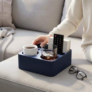 Könnte beinhalten: Ein marineblaues Sofatablett mit gerippter Textur, das eine weiße Kaffeetasse, ein Glas Whiskey, eine Fernbedienung und zwei weiße Blöcke enthält. Eine Brille mit schwarzem Rahmen liegt auf dem Sofa. Das Tablett dient zur Organisation von Gegenständen.