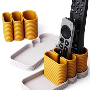 Könnte beinhalten: Ein senfgelber und weißer Fernbedienungsorganisator. Der Organizer hat drei Abschnitte für Fernbedienungen und zwei Ablagen. Der Text "Personalisierbar" befindet sich oben links. Zwei Fernbedienungen befinden sich im Organizer.