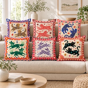 Puede incluir: Un conjunto de seis cojines cuadrados de tela color crema con ilustraciones coloridas de animales, incluyendo perros, tigres, leopardos, zorros, conejos y gatos, rodeados por bordes decorativos con patrones de estrellas y geométricos.