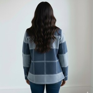 May include: A blue and grey plaid jacket with long sleeves. The jacket is worn by a person with long, dark hair. The jacket has a square pattern design and is made of a soft material. The person is wearing blue jeans.