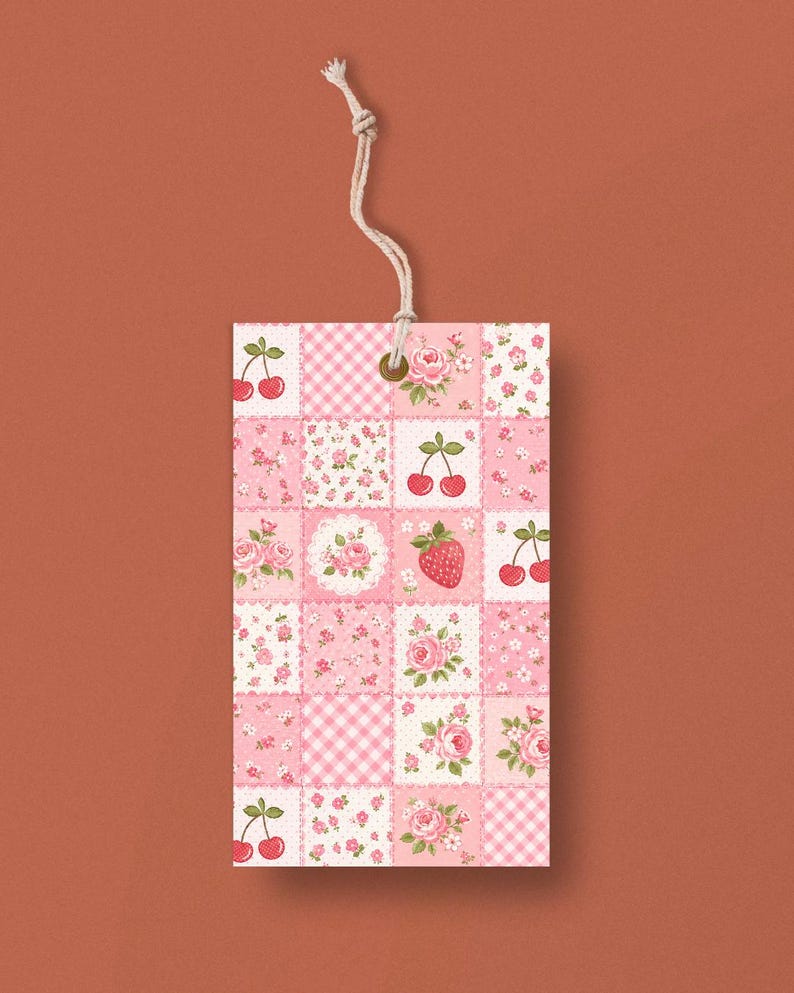 May include: A rectangular gift tag with a patchwork design featuring pink floral patterns, cherries, and a strawberry. The tag is made of paper and has a natural twine string attached for hanging.