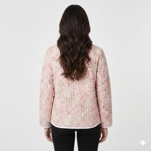 Op de afbeelding: Een roze gewatteerde jas met een bloemenpatroon. De jas heeft lange mouwen en een witte bies langs de kraag en manchetten. Het bloemmotief heeft tinten roze, cr&egrave;me en groen.