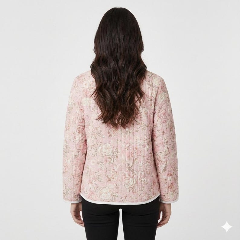 Op de afbeelding: Een roze gewatteerde jas met een bloemenpatroon. De jas heeft lange mouwen en een witte bies langs de kraag en manchetten. Het bloemmotief heeft tinten roze, cr&egrave;me en groen.