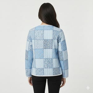 May include: A light blue quilted jacket with a patchwork design. The jacket features various shades of blue squares with floral and geometric patterns. It has long sleeves and a white trim along the neckline and hem.