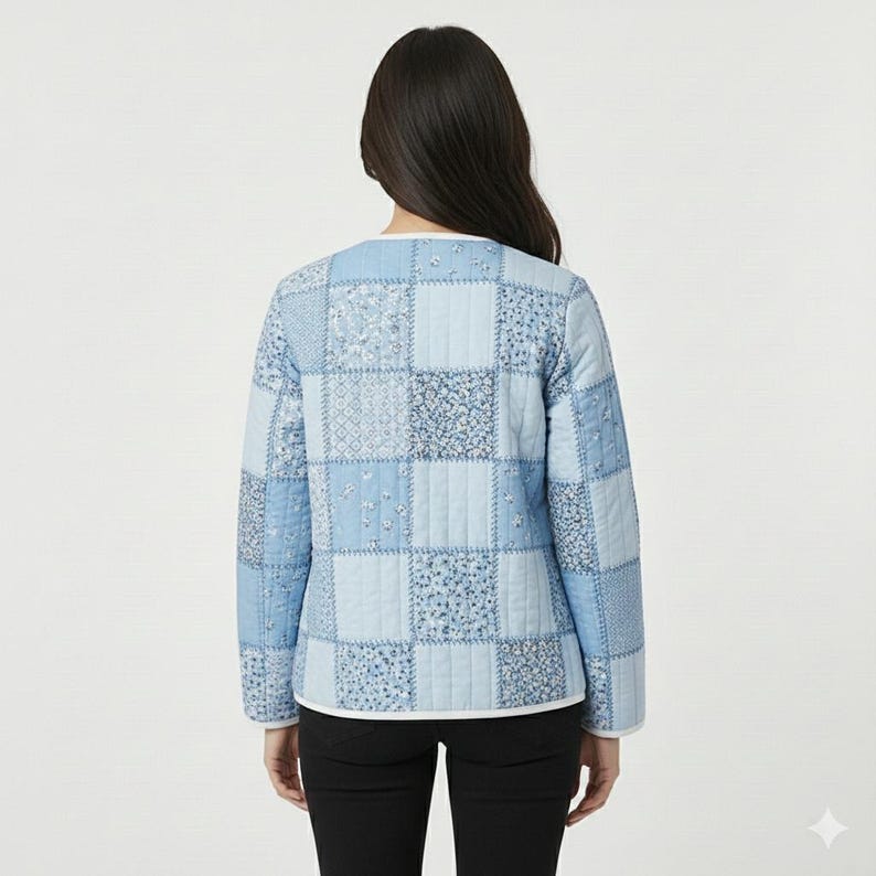 May include: A light blue quilted jacket with a patchwork design. The jacket features various shades of blue squares with floral and geometric patterns. It has long sleeves and a white trim along the neckline and hem.