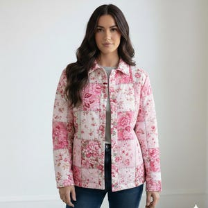 May include: A quilted jacket featuring a patchwork design with pink floral patterns on a white background. The jacket has a button-up front, a collared neckline, and long sleeves. The model is wearing blue jeans and a gray shirt underneath.