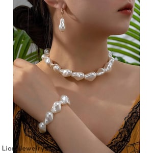 May include: A set of pearl jewellery comprising a necklace, bracelet, and earrings. The set features large, irregularly shaped white pearls. The earrings are teardrop-shaped, and the necklace and bracelet have a similar design.