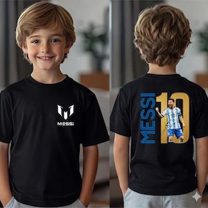 Może przedstawiać: Czarny t-shirt z białym logo "MESSI" z przodu. Tył koszulki przedstawia napis "MESSI" w kolorze niebieskim, numer 10 w kolorze złotym i zdjęcie piłkarza.