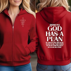 May include: A red zip-up hoodie with a white cross and the words "God Has a Plan" printed on the back. The hoodie has a front pocket and a hood. The text "Jeremiah 29:11" is above the main text.