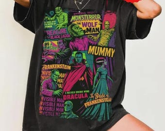 Puede incluir: Camiseta gris oscuro con un gráfico colorido de los monstruos clásicos de Universal. El diseño incluye imágenes de la Criatura de la Laguna Negra, Drácula, Frankenstein y la Momia. La camiseta también tiene el texto "MONSTERROR".