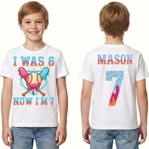 May include: White t-shirt with a colorful baseball-themed design. The front features the text "I WAS 6 NOW I'M 7" with a baseball and crossed bats. The back displays the name "MASON" and the number "7".