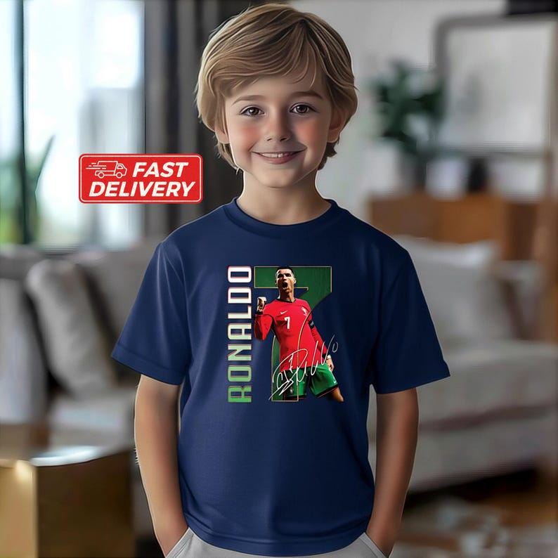 Puede incluir: Camiseta azul marino con un gr&aacute;fico de un jugador de f&uacute;tbol con una camiseta roja. Se ve el n&uacute;mero 7. La palabra "RONALDO" est&aacute; impresa verticalmente en verde y blanco. Una pegatina roja "FAST DELIVERY" est&aacute; en la esquina superior izquierda.