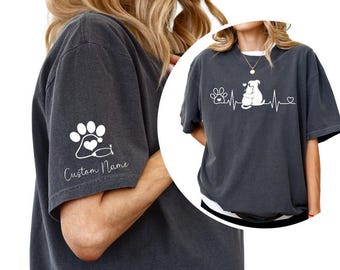 May include: A charcoal grey t-shirt featuring a white graphic of a heartbeat line with a paw print, a cat and dog hugging, and a small heart. The sleeve displays a white paw print icon with a stethoscope and the text Custom Name.