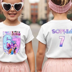 May include: White t-shirts with colorful graphics. One shirt features the text "I WAS 6 MONTHS" with a cartoon image. The other shirt has the name "SOPHIA" and the number "7" in a gradient font. Both shirts are worn by young children.