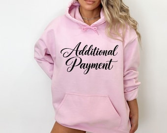 May include: A light pink hooded sweatshirt featuring the text Additional Payment printed in a black cursive script across the chest. The garment includes a front kangaroo pocket, long sleeves, and a drawstring hood with matching pink cords.