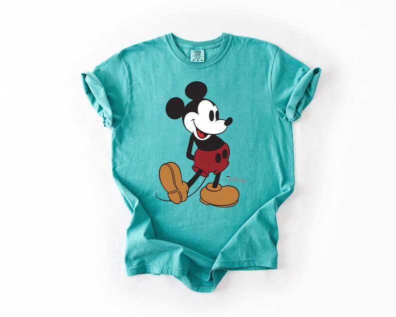 May include: A turquoise t-shirt featuring a graphic of Mickey Mouse. The cartoon character is depicted in his classic pose, wearing red shorts, yellow shoes, and black gloves. The shirt is made of a soft material and has a relaxed fit.