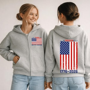May include: Two gray zip-up hoodies with the American flag design. The front of the hoodie has a small flag graphic with the text "FREEDOM" and "1776-2026". The back of the hoodie has a larger flag graphic with the same text.