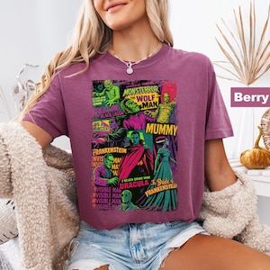 May include: Berry-colored t-shirt featuring a colorful graphic of classic movie monsters, including Frankenstein, the Mummy, and Dracula. The design includes the text "Monster Terror" and "The Wolf Man".
