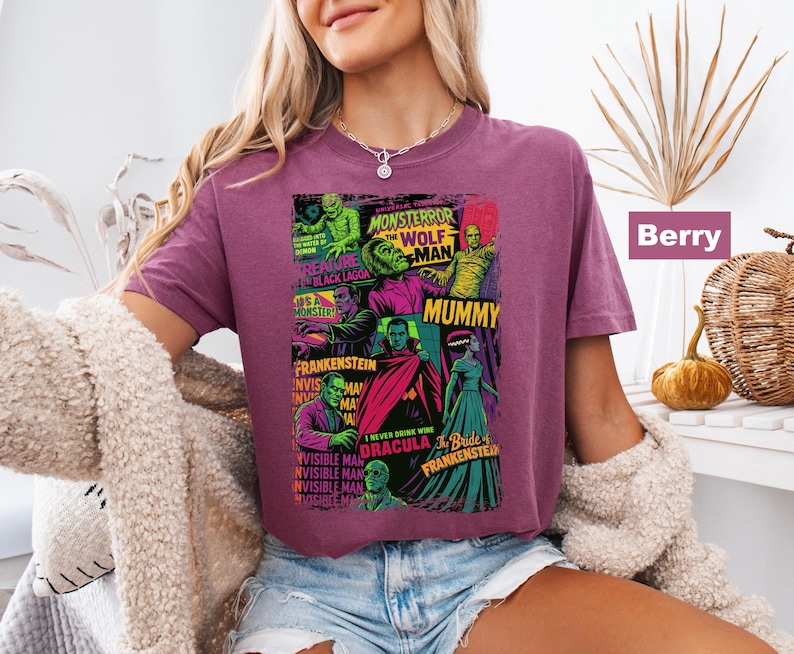 May include: Berry-colored t-shirt featuring a colorful graphic of classic movie monsters, including Frankenstein, the Mummy, and Dracula. The design includes the text "Monster Terror" and "The Wolf Man".