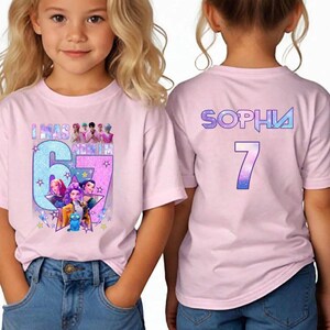 May include: Pink t-shirt with a colorful graphic featuring the text "I WAS 6 MONTHS" and a large number "67" with cartoon characters. The back of the shirt has the name "SOPHIA" and the number "7".
