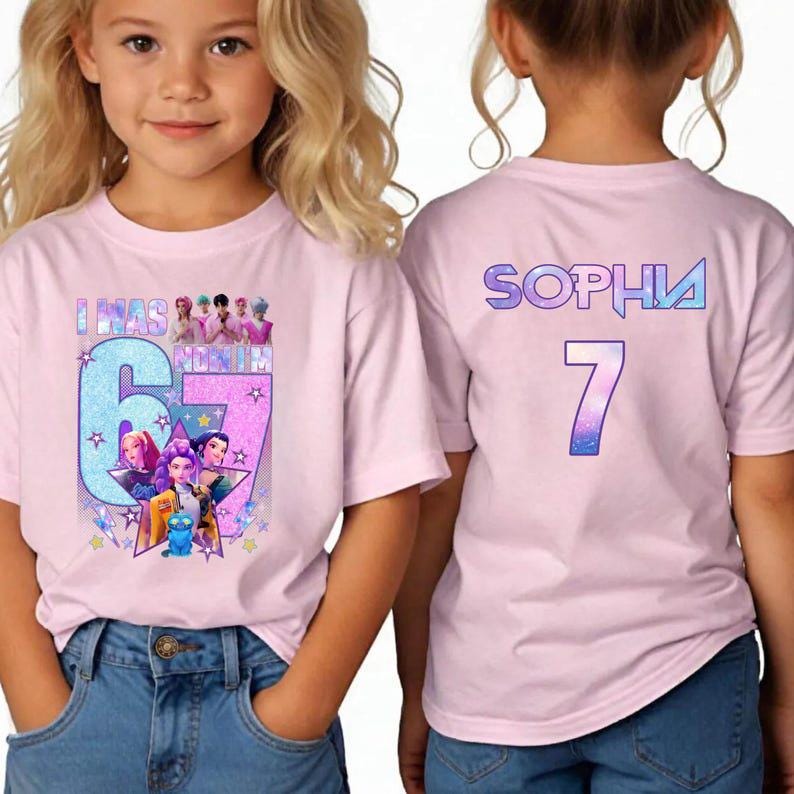 May include: Pink t-shirt with a colorful graphic featuring the text "I WAS 6 MONTHS" and a large number "67" with cartoon characters. The back of the shirt has the name "SOPHIA" and the number "7".