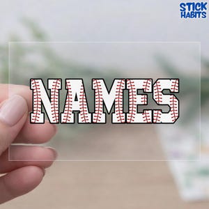 May include: A clear sticker with the word "NAMES" in a baseball-themed font. The letters are white with red stitching, mimicking a baseball. The sticker has a transparent border and the "STICK HABITS" logo is in the top right corner.