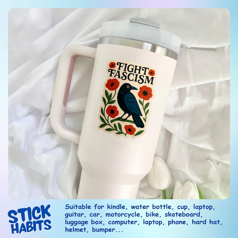May include: A white insulated tumbler with a handle, featuring a sticker that reads "FIGHT FASCISM." The sticker showcases a black bird, red flowers, and green leaves. The tumbler is designed for cold beverages.