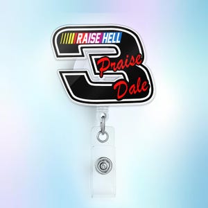 May include: A black and white badge reel with the number 3 design. The text "RAISE HELL" is above the number 3, and "Praise Dale" is written in red cursive. The reel has a clear plastic strap and a metal clip.
