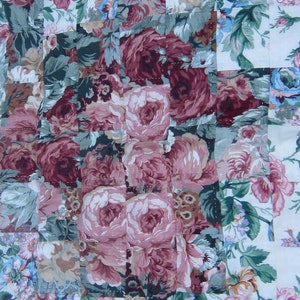 May include: A patchwork quilt with a floral pattern. The quilt is made of squares of fabric with different floral designs. The quilt is in shades of pink, green, and white.