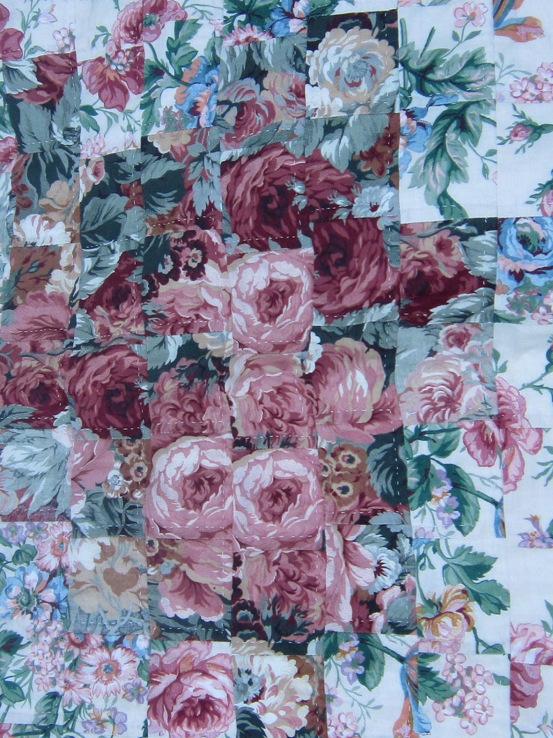 May include: A patchwork quilt with a floral pattern. The quilt is made of squares of fabric with different floral designs. The quilt is in shades of pink, green, and white.