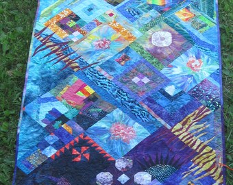 May include: A colorful quilt with a variety of patterns and textures. The quilt is made up of squares and triangles in shades of blue, purple, green, orange, and yellow. The quilt is edged in a dark purple fabric.