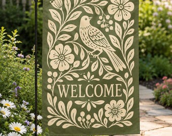 May include: A rectangular garden flag in olive green featuring a cream-colored screen-printed design of a bird perched on a branch surrounded by flowers and foliage. The word WELCOME is printed in a serif font in the center of the flag.