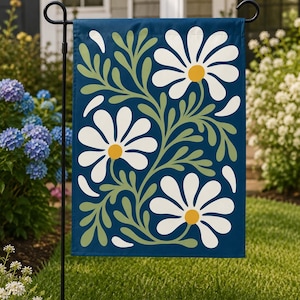May include: A rectangular garden flag featuring a deep blue background with a repeating pattern of three large white daisies with yellow centers. The flowers are connected by flowing sage green stems and leaves, accented by scattered white petals.