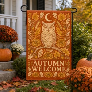 Puede incluir: Una bandera de jardín rectangular en tonos naranja y dorado con un búho central posado en una rama. El diseño incluye hojas de roble, bellotas y flores que rodean al búho, con una luna creciente arriba y el texto AUTUMN WELCOME.