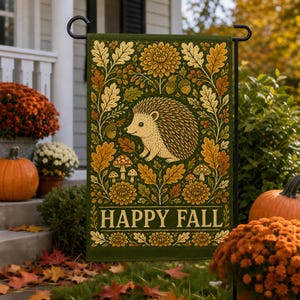 May include: A rectangular garden flag featuring a dark green background with a central illustration of a hedgehog surrounded by autumn leaves, acorns, mushrooms, and flowers. The text HAPPY FALL is printed in a light yellow font at the bottom.