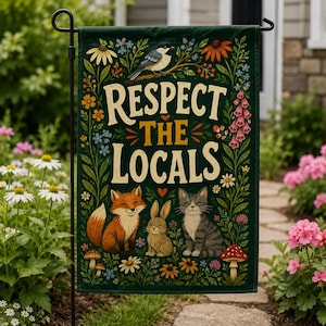 May include: A dark green garden flag featuring the text "RESPECT THE LOCALS" in cream and yellow lettering. The design includes a black-capped chickadee, a fox, a rabbit, and a tabby cat surrounded by colourful wildflowers and mushrooms.