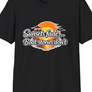 May include: Black t-shirt featuring a sunset graphic with the text "Sunsets fade... Boat stories don't" in white script. The graphic includes an orange sun and its reflection. A casual tee for boating enthusiasts.