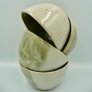 Peut inclure: Une pile de quatre bols en céramique aux teintes variées de vert et de blanc cassé. Les bols sont imbriqués, le bol supérieur étant partiellement ouvert, révélant l'intérieur. Les bols ont une texture tachetée et une finition brillante, suggérant de la poterie artisanale.
