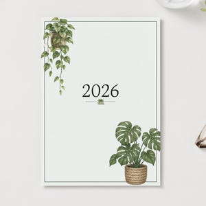 Peut inclure: Un calendrier 2026 rectangulaire avec un fond blanc et une fine bordure noire. Le design présente une plante verte suspendue dans le coin supérieur gauche et une plante monstera en pot dans un panier tressé en bas à droite.
