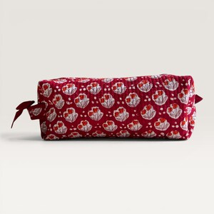 May include: A rectangular quilted pouch in a deep red fabric featuring a repeating pattern of white and orange floral motifs. The pouch has a structured shape with a fabric pull tab on the side, showcasing a consistent stitched texture throughout.