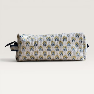 May include: A rectangular quilted pencil case featuring a repeating floral pattern in shades of yellow and blue on a white background. The case has a dark blue fabric zipper pull and a structured, boxy shape with visible stitching throughout.