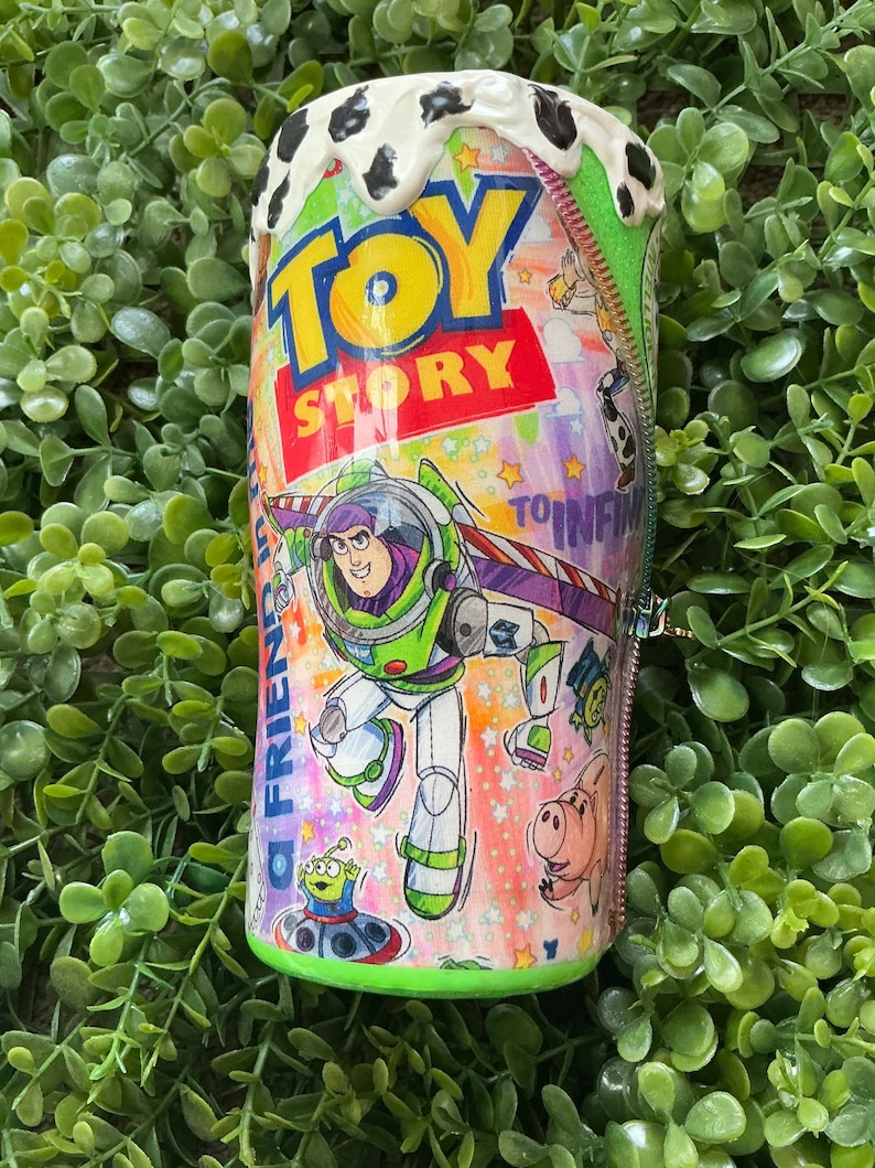 Peut inclure: Un gobelet avec des personnages du film d'animation "Toy Story". Le design comprend Buzz l'&Eacute;clair, les mots "Toy Story" et d'autres personnages. Le haut du gobelet pr&eacute;sente un motif tachet&eacute; blanc et noir.