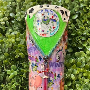 Peut inclure: Un gobelet avec un design color&eacute; inspir&eacute; du film Toy Story. L'int&eacute;rieur est vert et pr&eacute;sente un motif de fermeture &eacute;clair. Le dessus est orn&eacute; d'un motif tachet&eacute; noir et blanc avec le texte "NO SIGN OF INTELLIGENT LIFE ANYWHERE".