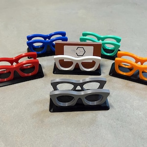 Glasses Business Card Holders sitting on concrete.  Colors are grey, blue, teal, red, white and orange.