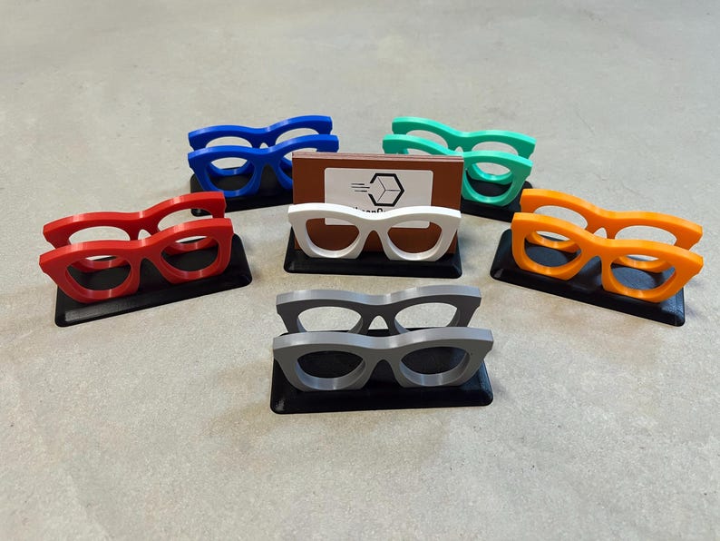 Glasses Business Card Holders sitting on concrete.  Colors are grey, blue, teal, red, white and orange.