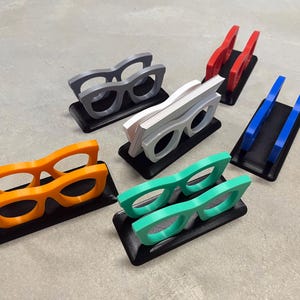 Glasses Business Card Holders sitting on concrete.  Colors are grey, blue, teal, red, white and orange.